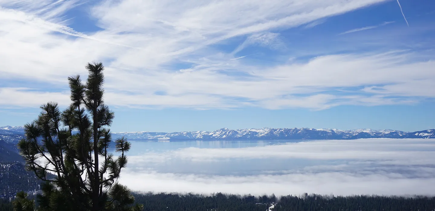 Lake Tahoe seen from the Nevada side, with the snow-capped Sierra Nevada beyond a low cloud layer